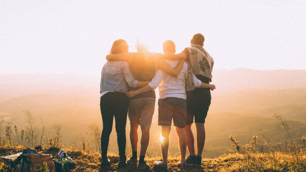 grupo de jóvenes abrazándose con el sol de fondo