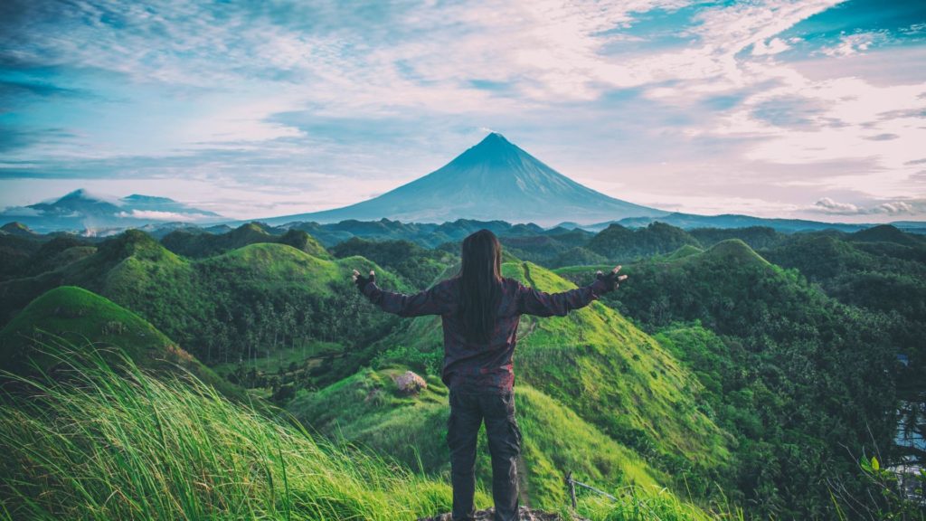 persona mirando un paisaje verde con una gran montaña al fondo